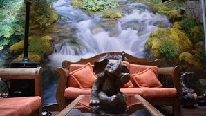 Una habitación acogedora con un mural de un río serpenteante, un sofá de madera con cojines naranja y una mesa de centro de cristal con una figurita decorativa de elefante.