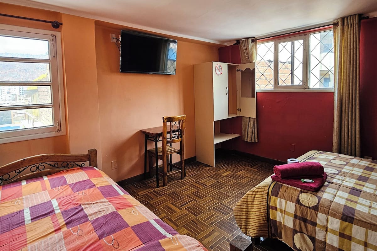 A hotel room with two beds, a TV, a wardrobe, and a window with a city view.