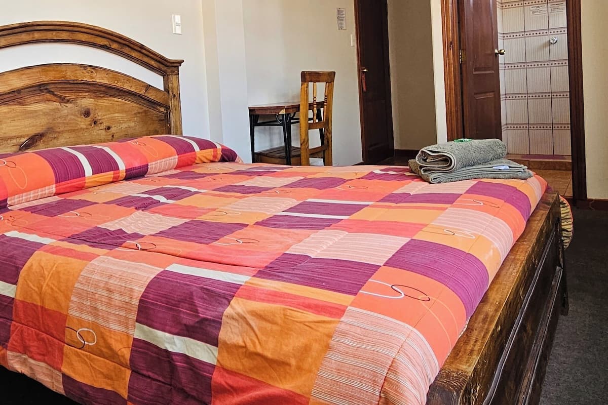 A bedroom with a wooden bed, a chair, a small table, and a wardrobe with a mirror.