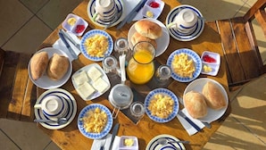 Una mesa de desayuno con platos de huevos, tostadas y pasteles, junto con tazas y una jarra de jugo.
