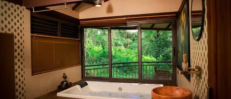 Ein Badezimmer mit einer großen Badewanne, einem Holzeimer und einem Fenster mit Blick auf Grünflächen.