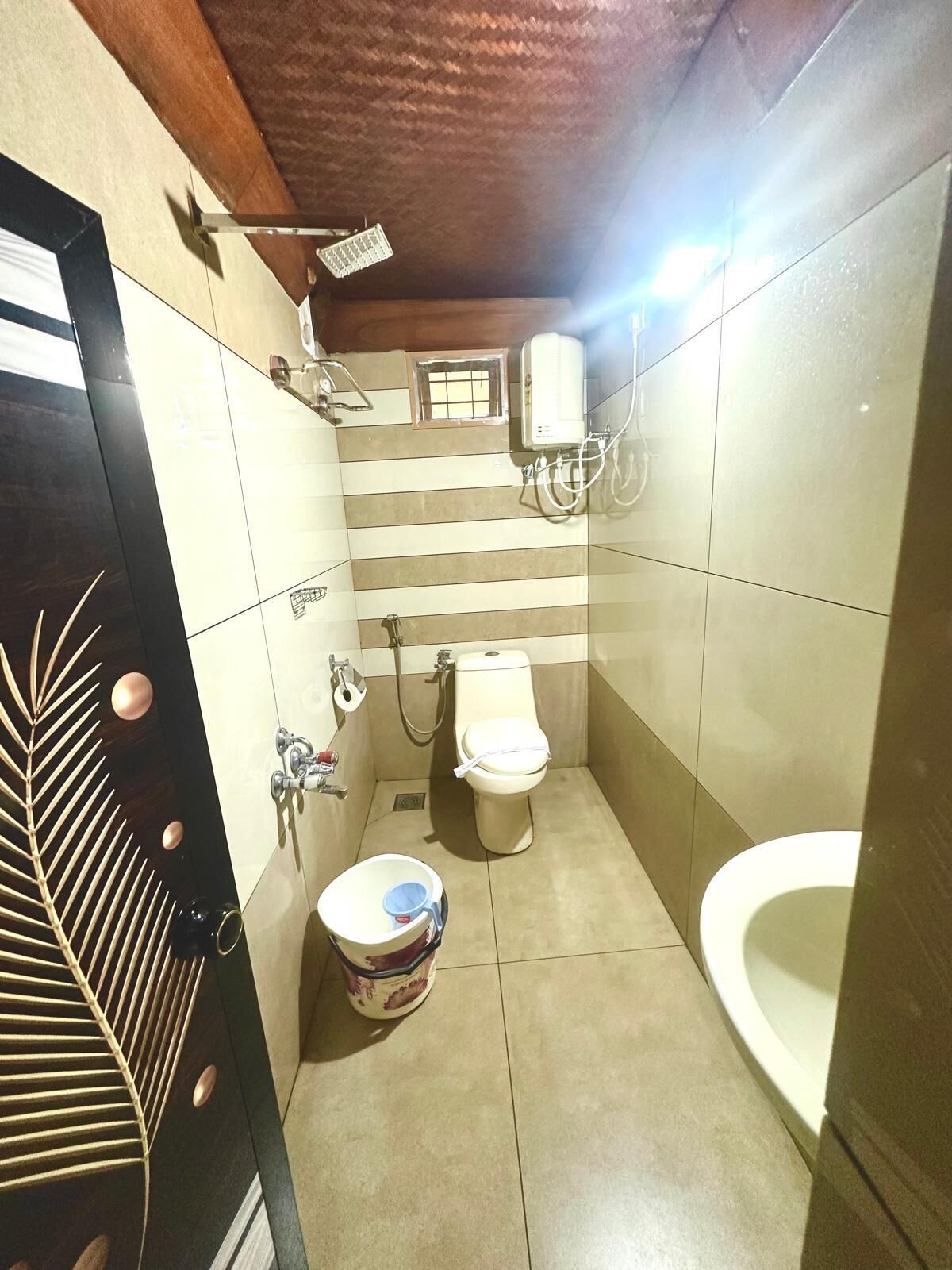 A small bathroom with a toilet, bidet, and sink. There is a showerhead above the toilet and a small window above the bidet.