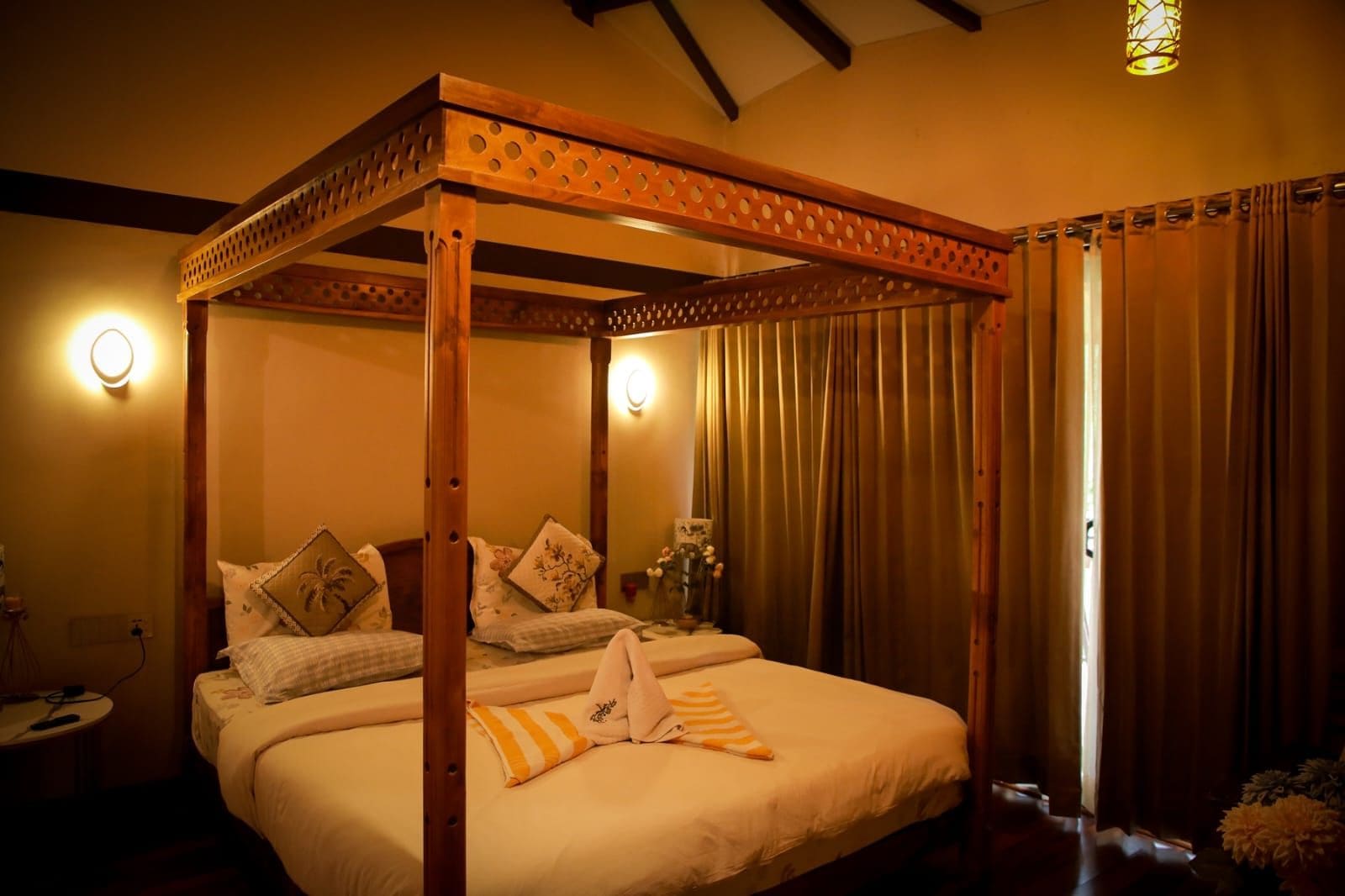 Een hemelbed met een baldakijn, een nachtkastje met een lamp, en uitzicht op de omgeving door gordijnen.