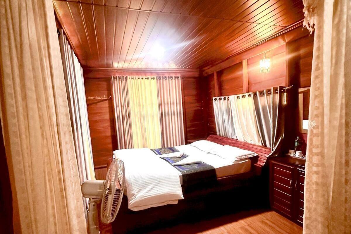 A wooden cabin room with a bed, a fan, and a small cabinet.