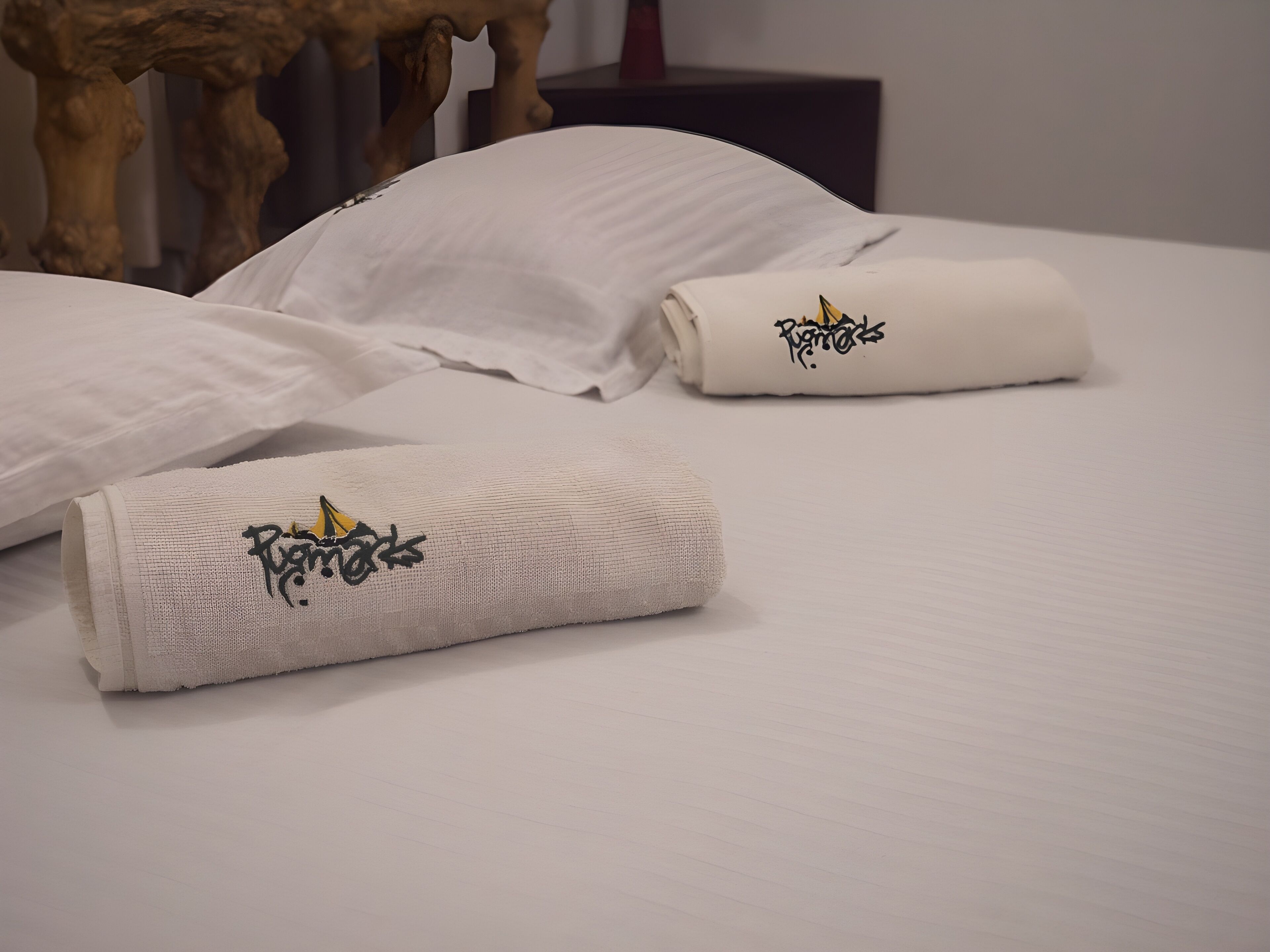 A neatly made bed with white linens and two towels with embroidered text.