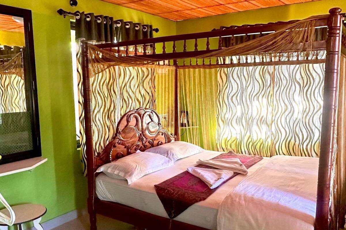 A four-poster bed with a wooden headboard, a green wall, and a mirror on the left.