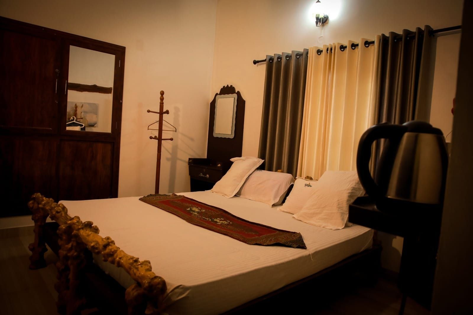 A room with a bed, a chair, a wooden wardrobe, a mirror, and a window with curtains.