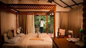 A bedroom with a bed, curtains, a wooden chair, a table with a vase, and a balcony with a person.