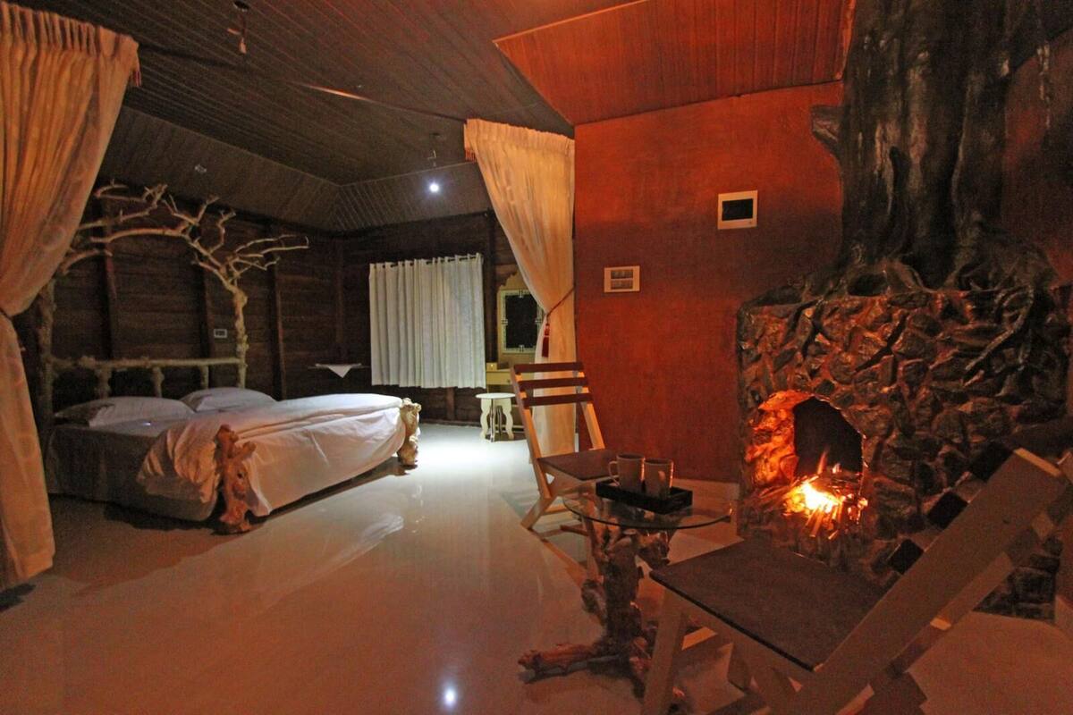 A cozy room with a bed, a table with a fire, and a stone wall.