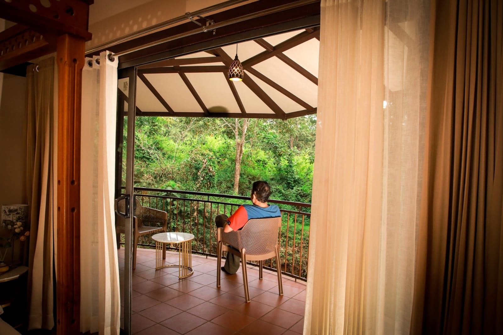 A balcony with a person seated at a table, surrounded by a railing and curtains.