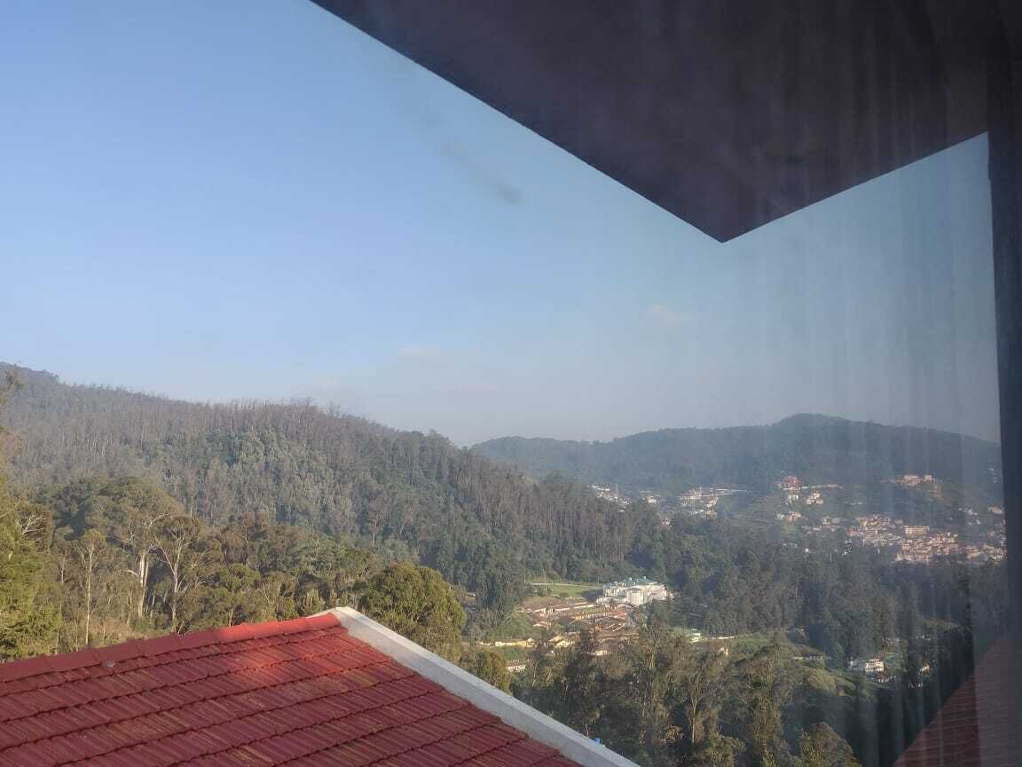 A view from a window overlooking a forested valley with a red-roofed building in the foreground.