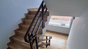 Un escalier avec des marches en bois et des rampes noires, menant à une pièce dotée d’une fenêtre et offrant une vue sur l’extérieur.