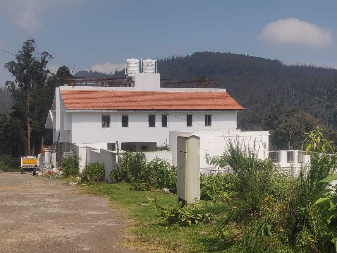 A white building with a red roof, surrounded by greenery and a hilly landscape.