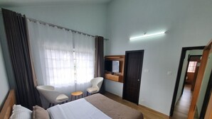 Une chambre d’hôtel comprenant un lit, deux chaises, une petite table, un téléviseur et une armoire.