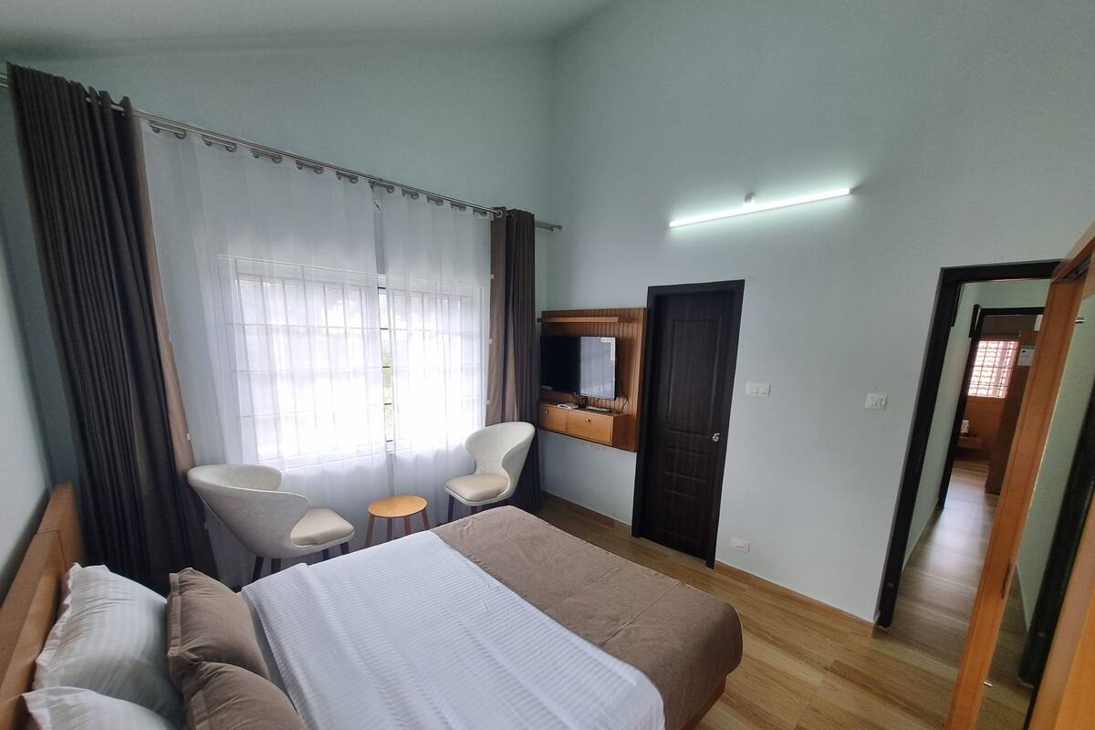 A hotel room with a bed, two chairs, a small table, a TV, and a wardrobe.
