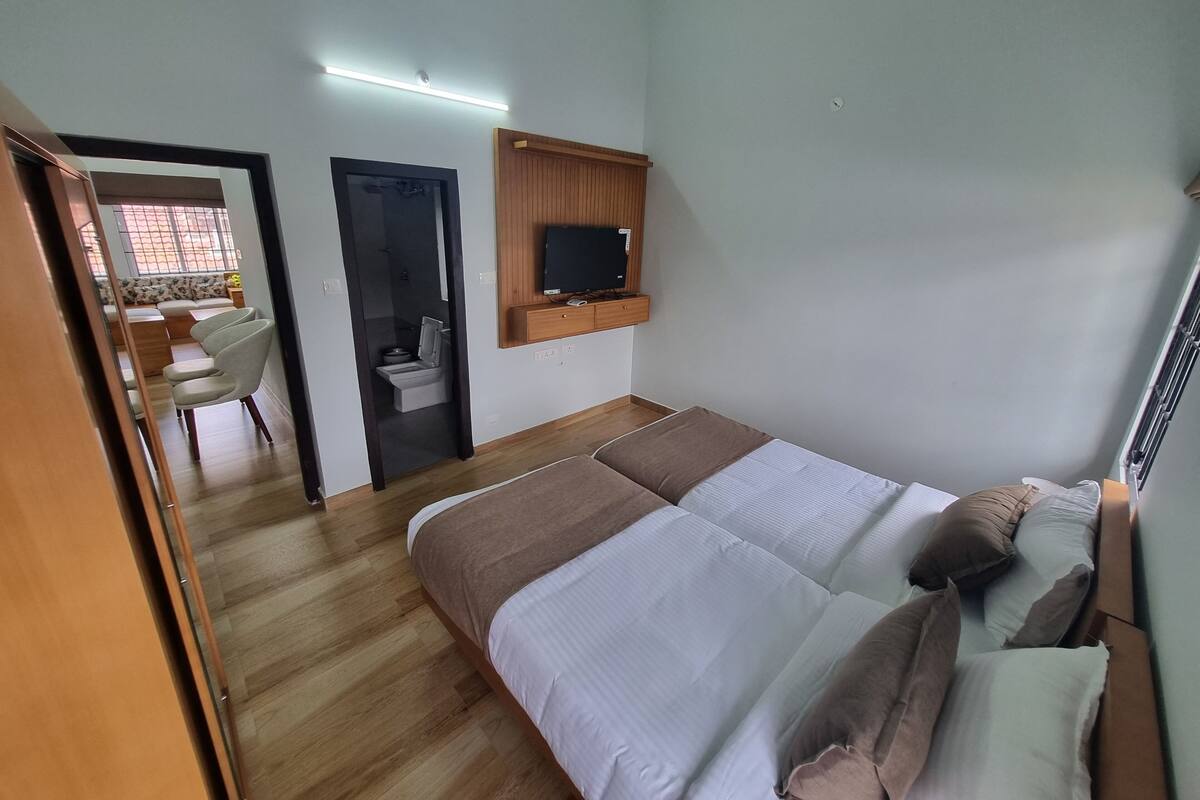 A bedroom with a bed, a TV mounted on the wall, a wooden desk, and a chair.
