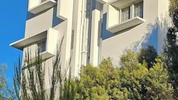 Un immeuble moderne à plusieurs étages, doté de balcons et entouré de verdure.