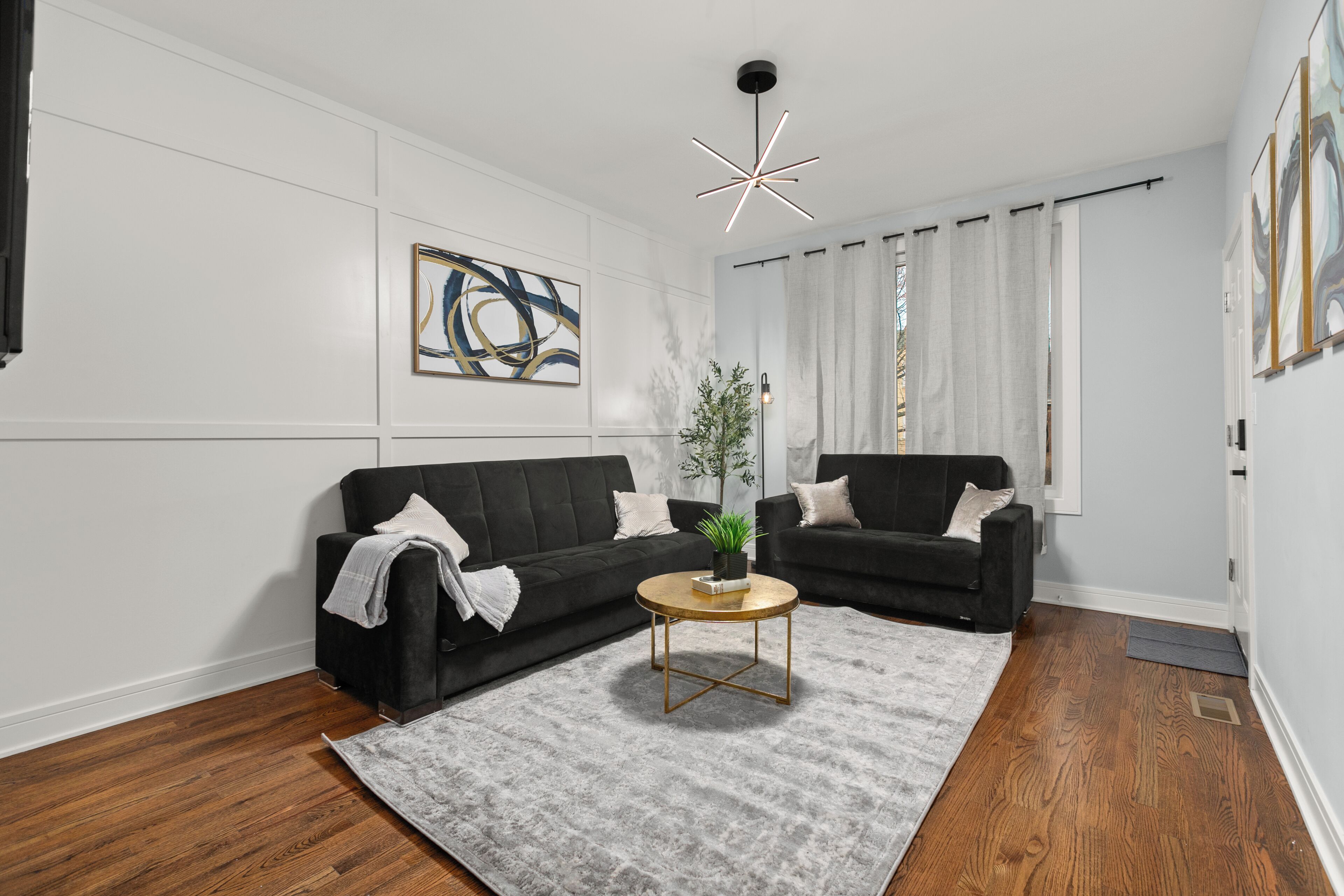 Ein modernes Wohnzimmer mit zwei schwarzen Sofas, einem runden Couchtisch, einem grauen Teppich und einer zeitgemäßen Leuchte.