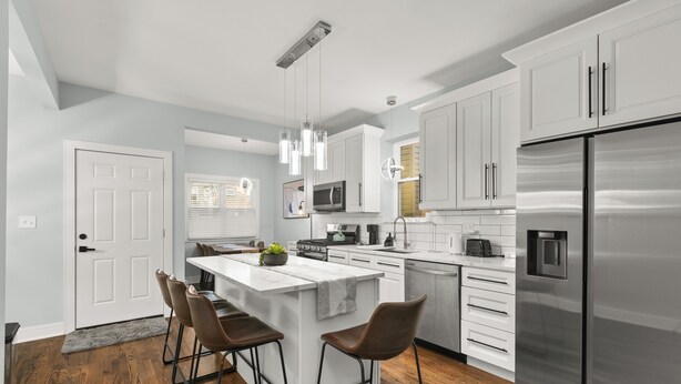 A modern kitchen with white cabinets, stainless steel appliances, and a central island with bar stools. - Luxury 5Bed 2Bath Apt w/Parking (Chicago)