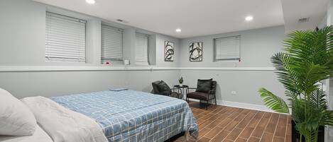 Une chambre à coucher avec un lit, une petite table, deux chaises, une plante en pot et des œuvres d’art accrochées aux murs.