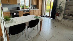 A modern kitchen with wooden cabinets, a dining table with chairs, a built-in oven, and a large window.