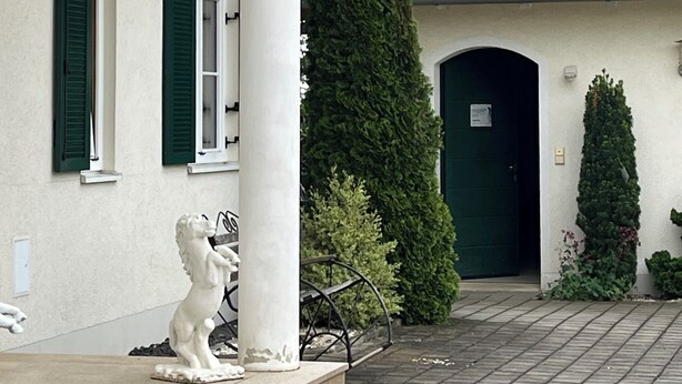 A building with a tiled roof, a green door, and a statue on the front steps.