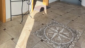 A room with a tiled floor, a desk with a chair, a mirror, and a door leading to another room.