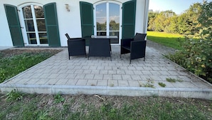 A patio with a table and chairs, a covered area, and a view of the surrounding greenery.