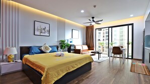 A modern hotel room with a large bed, a desk, a chair, a ceiling fan, and a view of the city through the balcony.
