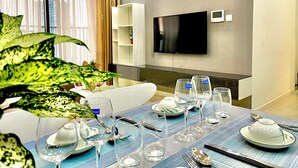 A modern dining area with a table set for four, a television mounted on the wall, and a large window with curtains.