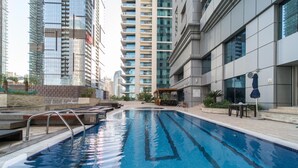A swimming pool with clear blue water, surrounded by modern buildings and a covered seating area. - Impressive 2BR at Princess Tower (Dubai)