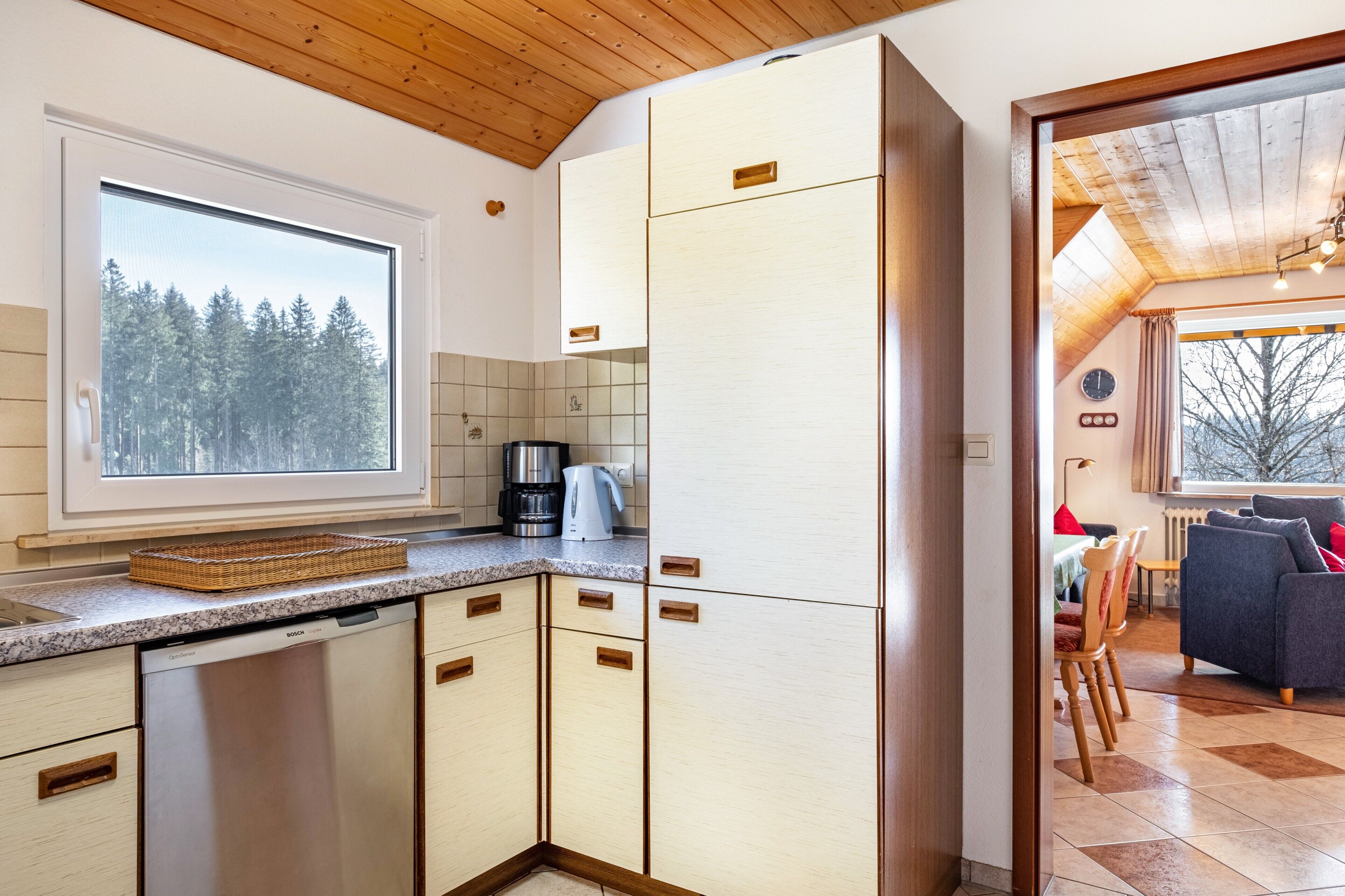 Eine moderne Küche mit Geschirrspüler, Kaffeemaschine und einem Fenster mit Blick auf den Wald.