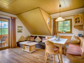 Een gezellige kamer met een houten plafond, een eettafel, een bank en een raam met uitzicht op bomen.
