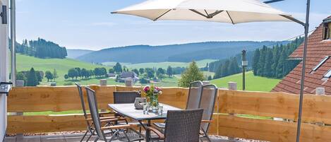 Een terras met een tafel en stoelen, een houten hek en uitzicht op een groen landschap.