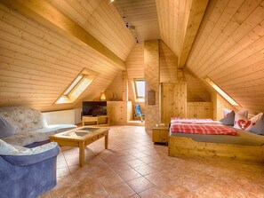 Une pièce mansardée chaleureuse avec des murs en bois, une télévision, un canapé, un lit et une petite table.
