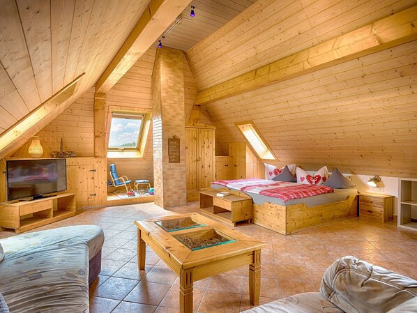 Une chambre mansardée chaleureuse avec un plafond en pente en bois, un lit, une télévision et une petite table.