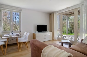 A modern living room with a TV, white furniture, and large windows.