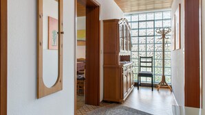A hallway with a wooden cabinet, a coat rack, and a large window with a view of trees. - Apartment 'Säntis, 50qm' with Balcony and Wi-Fi (Mühlingen)