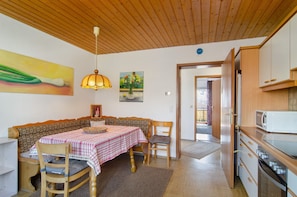 A dining area with a table set for two, a wooden ceiling, and a kitchen area with cabinets and a microwave. - Apartment 'Säntis, 50qm' with Balcony and Wi-Fi (Mühlingen)