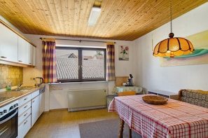 A kitchen with a window, a dining table with a checkered tablecloth, and a hanging lamp. - Apartment 'Säntis, 50qm' with Balcony and Wi-Fi (Mühlingen)