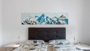 A bedroom with a bed, two bedside tables, a nightstand, a headboard, and a painting of mountains. - Apartment 'Säntis, 50qm' with Balcony and Wi-Fi (Mühlingen)