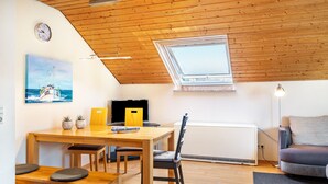 Una habitación acogedora con techo de madera, una mesa de comedor con sillas, un sofá, un radiador y un cuadro de un barco en la pared.