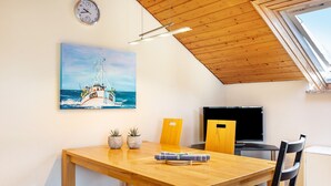 Un comedor con una mesa de madera, sillas, un reloj, un cuadro de un barco y un televisor.