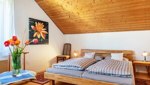 Un dormitorio con techo de madera, una cama con ropa de cama a rayas, una mesita de noche con lámpara y un cuadro en la pared.