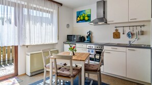 A compact kitchen with a dining area, a radiator, a microwave, a stove, and a large window with sheer curtains.