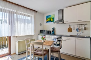 Una cocina compacta con comedor, un radiador, microondas, estufa y un amplio ventanal con cortinas ligeras.