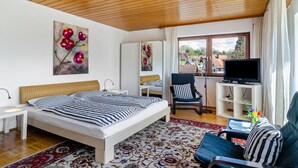 A bedroom with a bed, a chair, a TV, and a window.