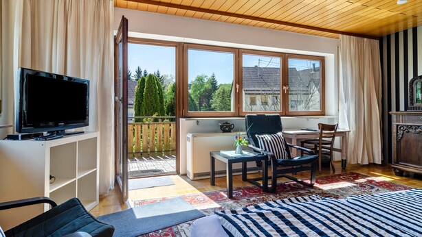 A living room with a TV, a sofa, a chair, a table, and a view of the outside.