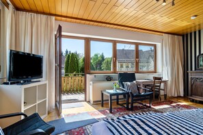 Una sala de estar con televisor, sofá, sillón, mesa y vistas al exterior.