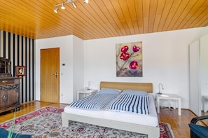 Un dormitorio con cama, mesitas de noche, techo de madera, una puerta y un cuadro.